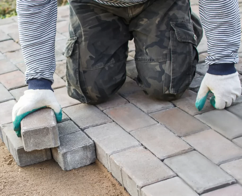 Stenläggning. Stenläggare Örebro. Man på knä med stenblock